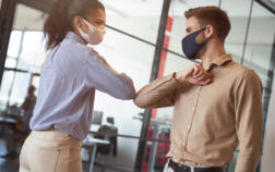 Two young diverse business colleagues wearing face protective masks bumping elbows, greeting each other while working during covid 19 quarantine Social distancing at work. Two young diverse business colleagues wearing face protective masks bumping elbows, greeting each other while working during covid 19 quarantine. Preventing coronavirus