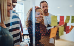 Smiling designers having a brainstorming session in an office Smiling group of designers reading sticky notes on a glass wall during a brainstorming session together in a modern office